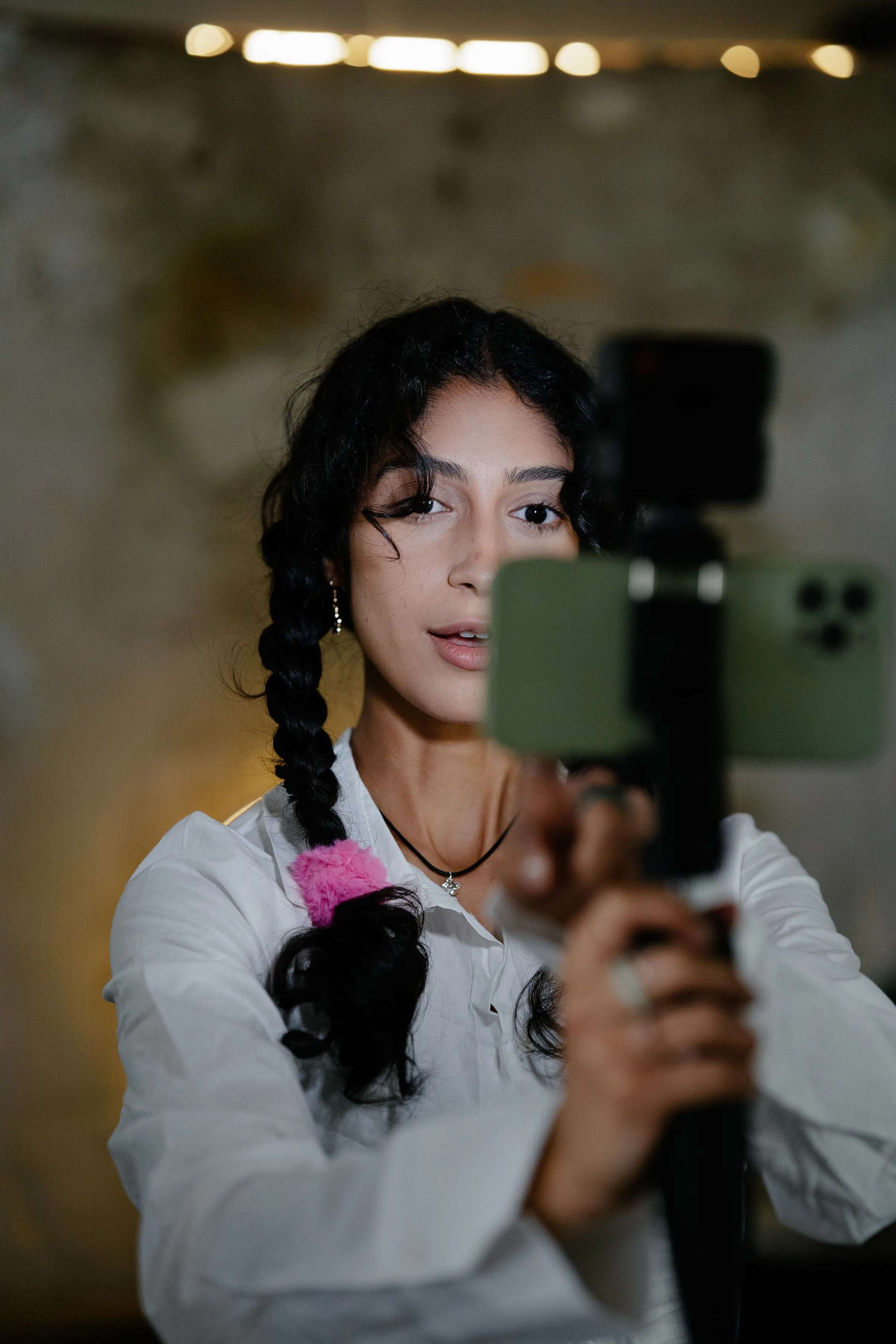 Woman with braided hair uses smartphone stabilizer indoors for recording.