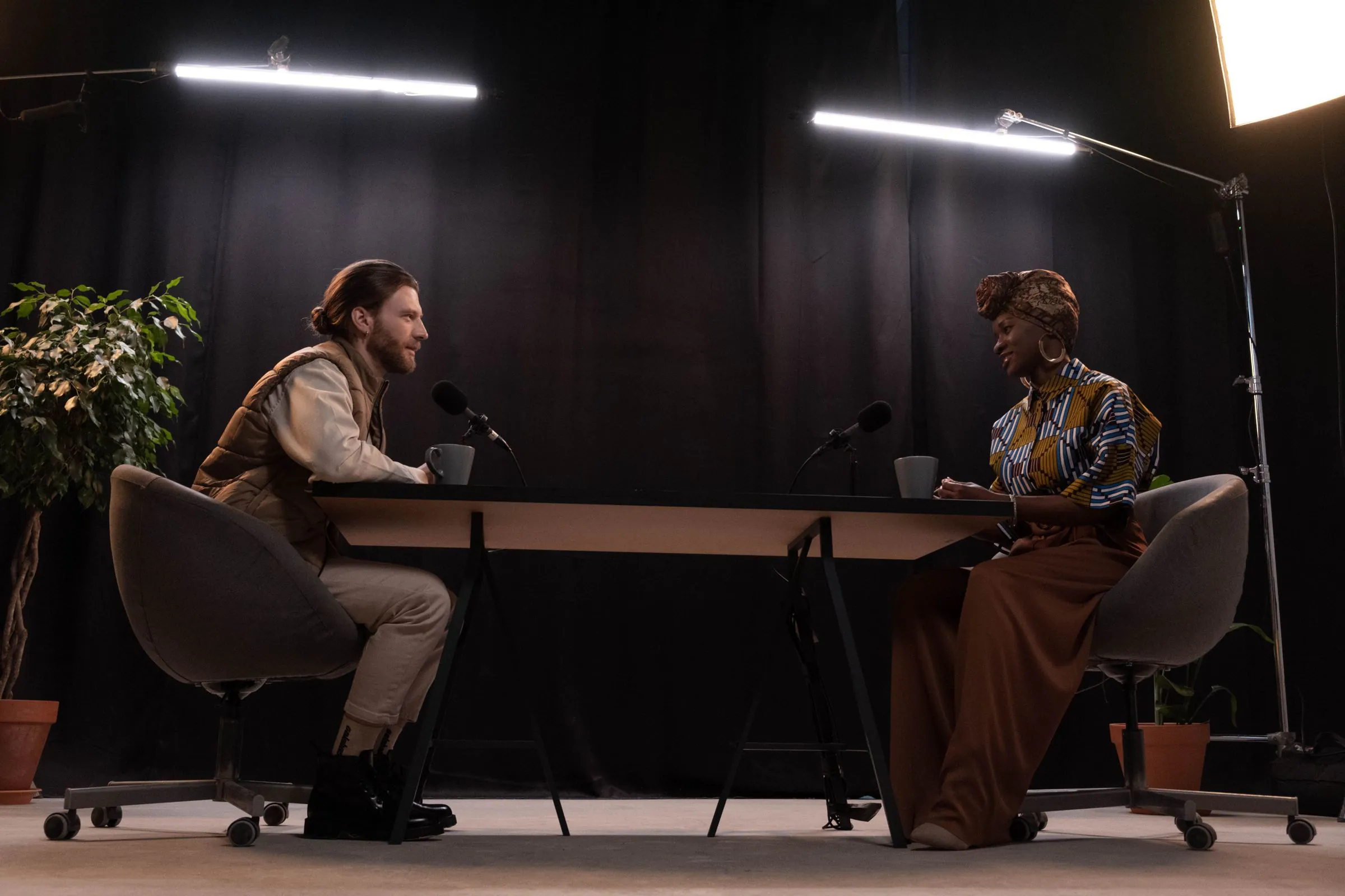 A man and woman recording a podcast in a professionally lit studio with microphones.