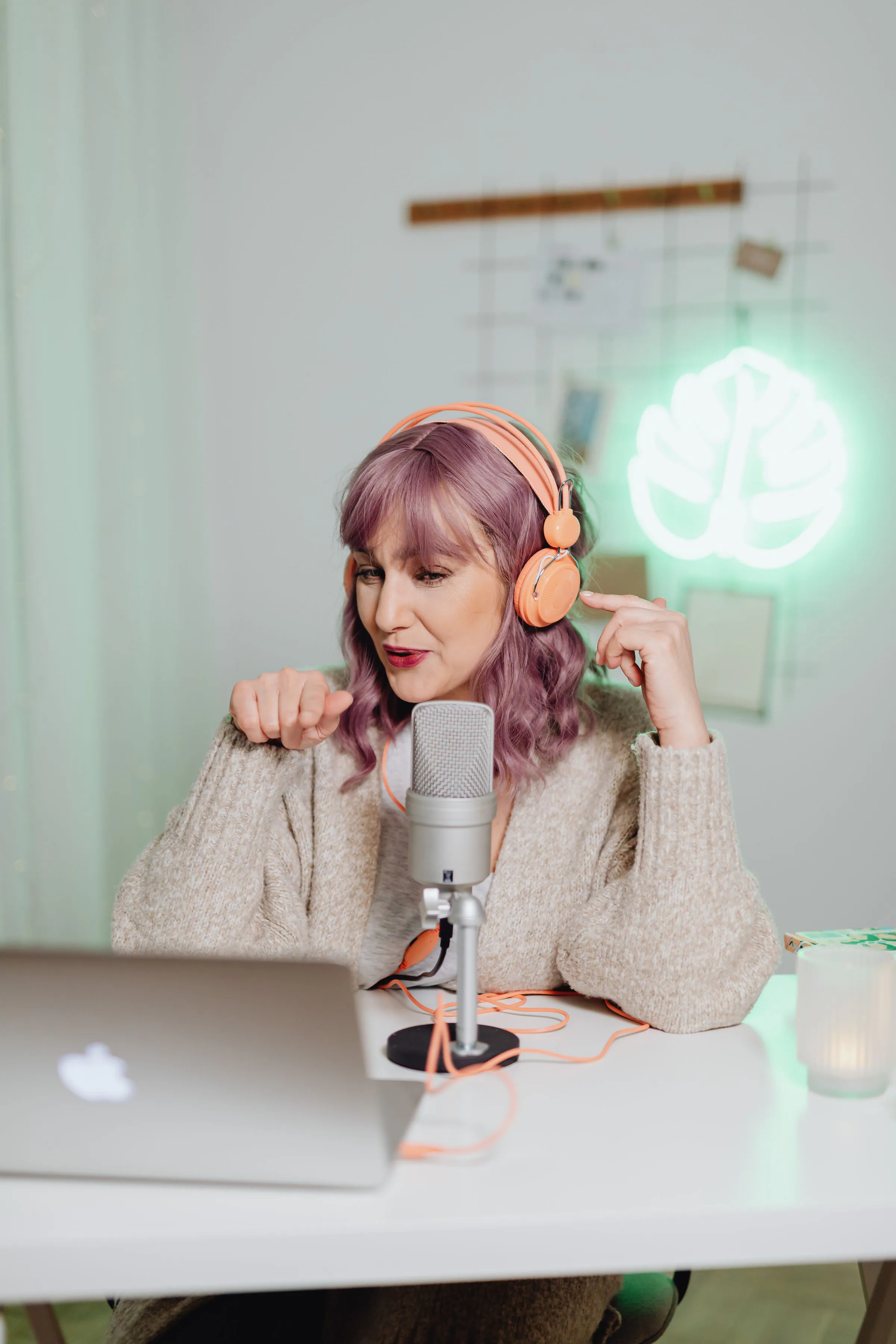 A woman recording a podcast indoors with a laptop and microphone, wearing headphones.