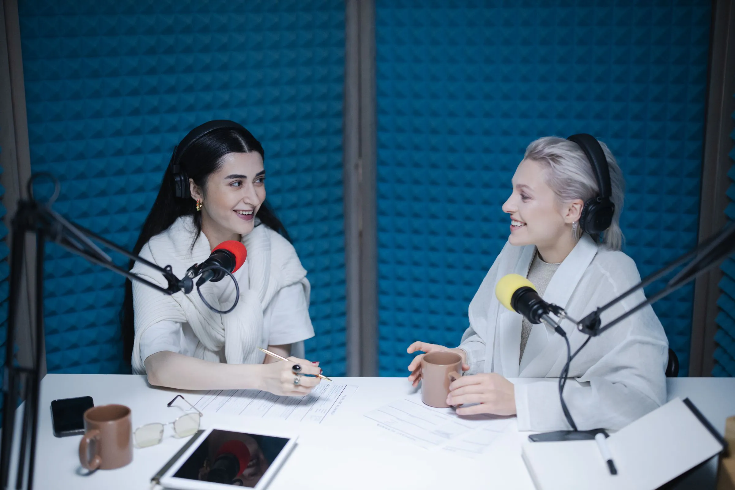 Two women engaged in a lively podcast discussion inside a professional studio setting.